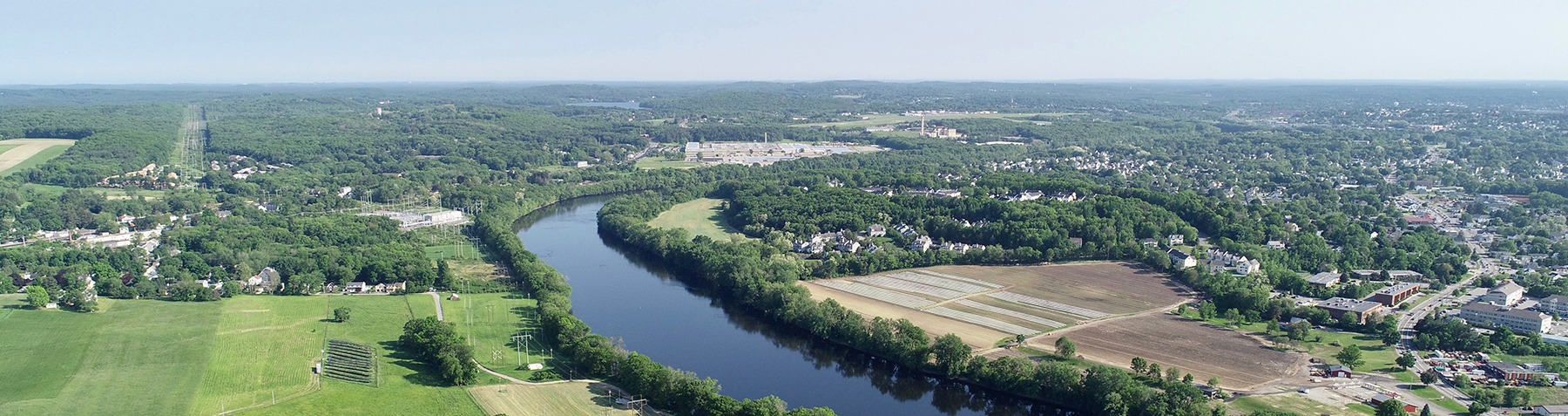 Aerial view of a winding river flowing through green fields and farmland under a clear sky.