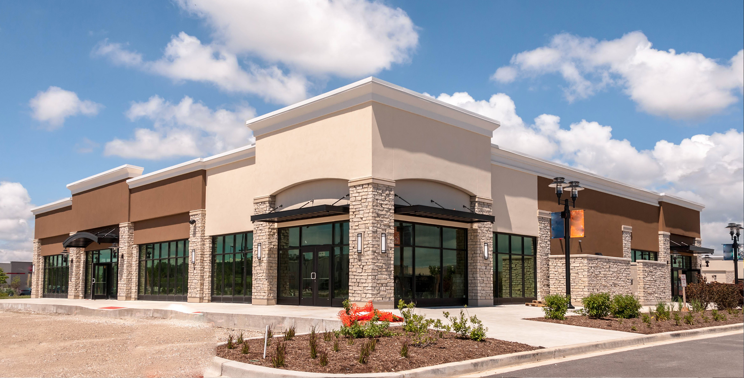 Single-story commercial building with brick and stucco exterior, large windows, and a parking lot under a clear blue sky.