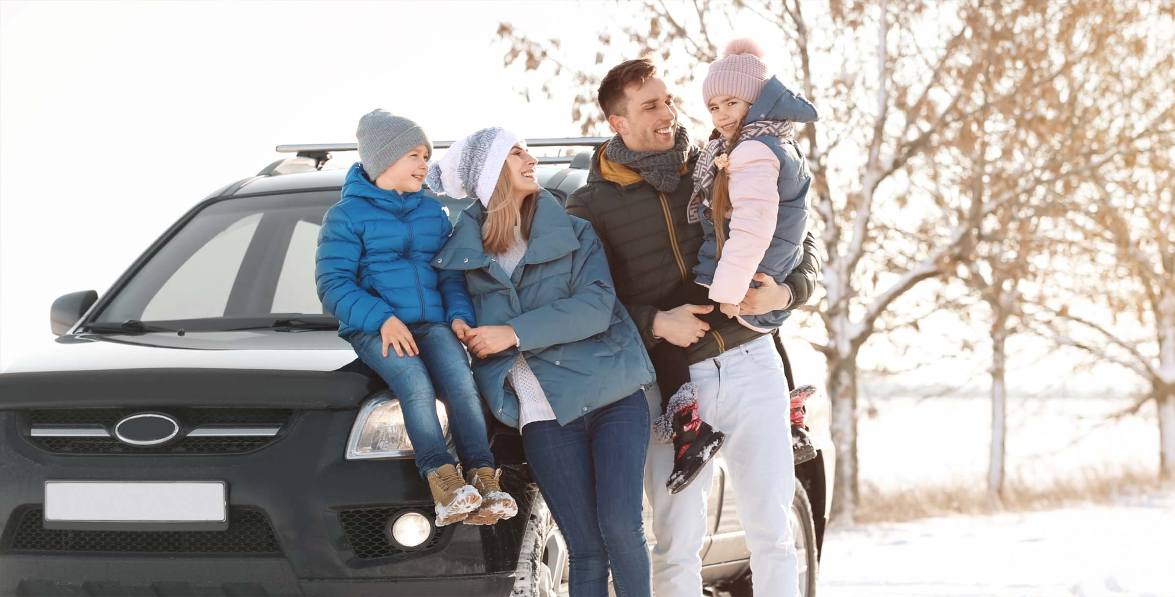 Smiling family standing beside a car in a winter setting, dressed in warm clothing, suggesting safe travel and family auto protection.