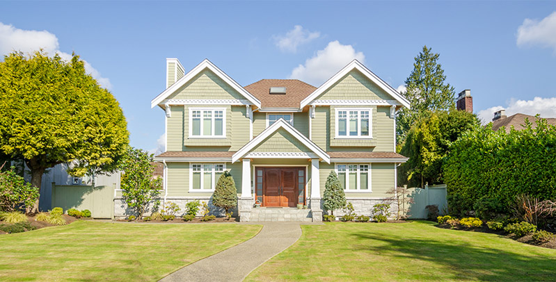 a large, two-story residential single-family home featuring sage green siding, white trim, and a prominent stone foundation around the base